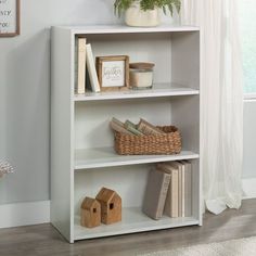 a white book shelf with books and plants on top