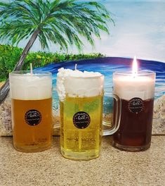 three beer mugs sitting on top of a counter next to a candle and palm tree