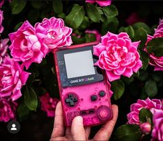 a person holding a pink game boy color in their hand next to some pink flowers