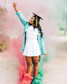 a woman in a graduation cap and gown is holding her hand up to the sky