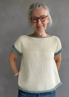 an older woman wearing glasses standing in front of a gray wall with her hands on her hips