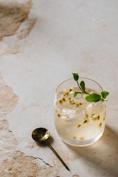 a glass filled with ice and mint sitting on top of a table next to a spoon