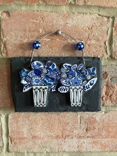 two blue and white flowers are hanging on a brick wall next to a pair of earrings