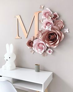 a white desk topped with a wooden letter and pink flowers on it's wall