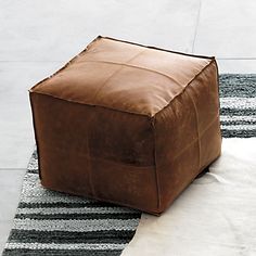 a square leather ottoman sitting on top of a rug