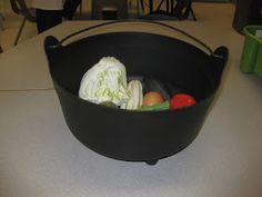 a black basket filled with assorted vegetables on top of a white table next to green bins