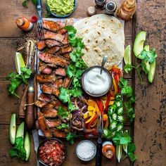 an assortment of food is laid out on a wooden table with utensils and condiments