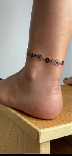 a woman's bare foot with a tattoo on the side of her leg, sitting on a wooden table