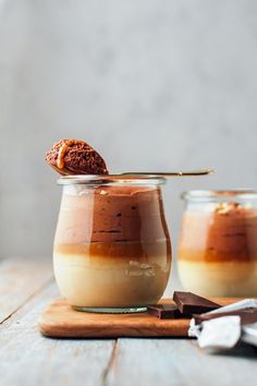 two jars filled with desserts sitting on top of a wooden table next to a spoon