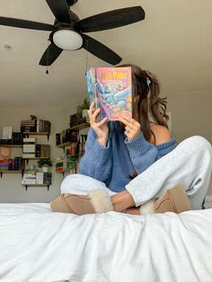 a woman sitting on top of a bed holding a book in front of her face