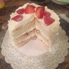 a white cake with strawberries on top is cut in half to show the layers