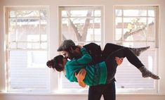 a man holding a woman in his arms while standing next to a window with two windows behind them