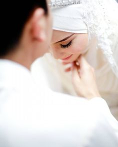 a woman wearing a white veil and holding her hand to her face while looking at herself in the mirror