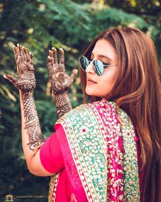 a woman with henna on her hands and sunglasses looking up at the trees in the background