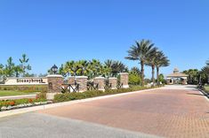 the entrance to an apartment complex with palm trees and flowers on either side of it