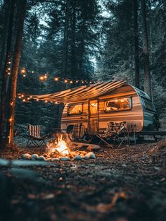 a camper parked in the woods next to a fire with lights strung from it