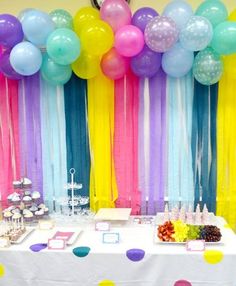 a table topped with lots of balloons next to a wall filled with colorful streamers