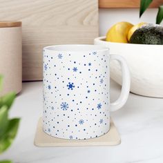 a white and blue coffee mug sitting on top of a counter next to a bowl of fruit