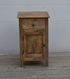 a small wooden cabinet sitting on top of a hard wood floor next to a white wall