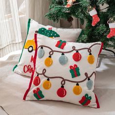 two christmas pillows sitting on top of a bed next to a christmas tree and stockings