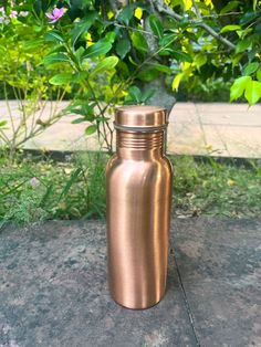 a metal bottle sitting on top of a cement ground next to some bushes and trees