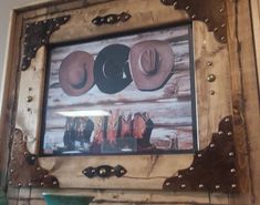 a wooden frame with cowboy hats hanging on it's wall above a green vase