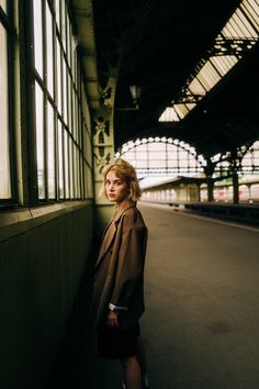 a woman standing in front of a window next to a train station with lots of windows