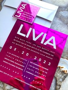 a pink and white wedding card with the word livva printed on it next to some rocks