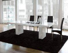 a white table with black chairs in front of large windows and a rug on the floor