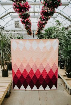 a pink and red quilt hanging from a ceiling in a greenhouse with potted plants