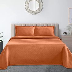 an orange bedspread and pillows in a white room with a mirror on the wall