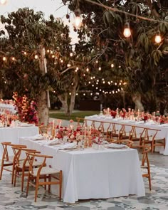 an outdoor dinner table set up with white linens and wooden chairs, surrounded by string lights