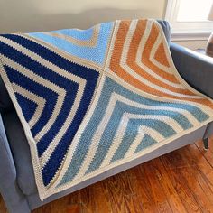 a blue and orange crocheted blanket sitting on top of a gray couch next to a window