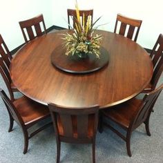 a round wooden table with six chairs and a flower vase on the top, in front of a white wall