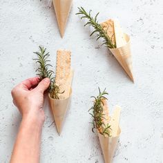 four cones with herbs and crackers in them on a white surface, being held by a person's hand