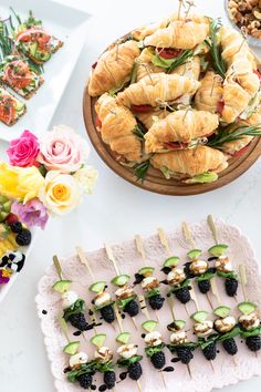 an assortment of appetizers are displayed on trays with flowers in the background