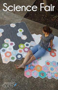 a woman sitting on the ground next to a quilt