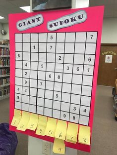 a giant sudoku board in the middle of a library with yellow sticky notes on it