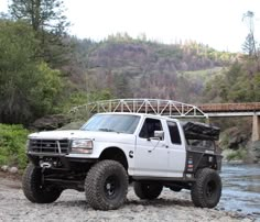 a white truck parked on the side of a river next to a bridge and trees