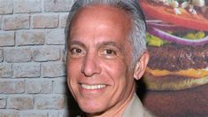 a smiling man in front of a brick wall with a large hamburger on it's side