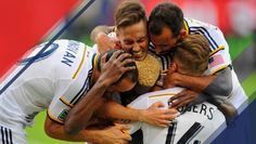 a group of soccer players hugging each other in the middle of a hug with an american flag background