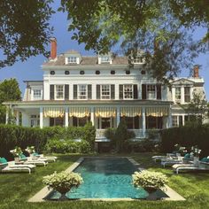 a large white house with a pool in the front yard and lawn chairs around it