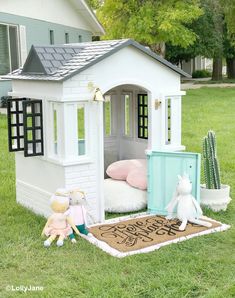 a small white doll house sitting on top of a grass covered field next to a cactus