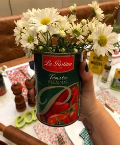 a person holding up a can with flowers in it