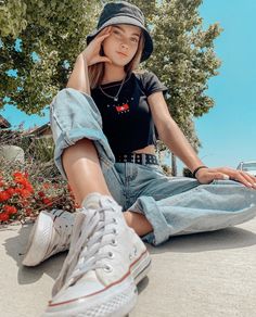 a young woman sitting on the ground with her legs crossed and wearing white tennis shoes