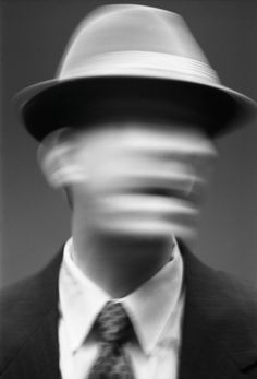 a blurry image of a man wearing a suit and tie with a hat on his head