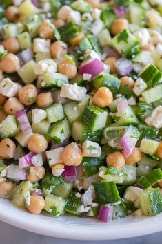 a salad with chickpeas, cucumbers and onions in a white bowl