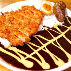 a white plate topped with rice covered in sauce and meat next to an egg on top of it