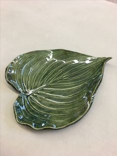 a green leaf shaped dish sitting on top of a white tablecloth covered floor next to a wall