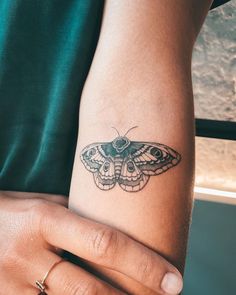 a moth tattoo on the arm of a person's left hand, with an eye patch in the middle